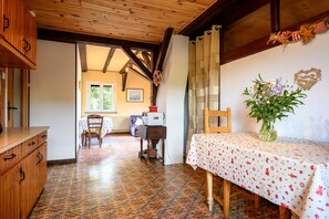 Una habitación con techo de madera, una mesa de comedor con mantel blanco, un jarrón con flores y un aparador de madera.