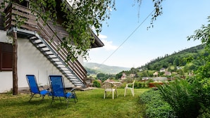 A house with a sloped roof, a wooden staircase, and a view of a green valley.