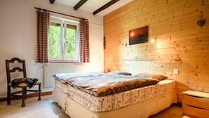 A bedroom with a wooden wall, a bed, a chair, and a window with curtains.