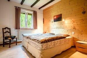 A bedroom with a wooden wall, a bed, a chair, and a window with curtains. - Apartment “Au Petit Chamois” with Mountain View, Private Garden and Wi-Fi (Breitenbach-Haut-Rhin)
