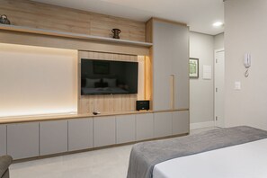Quarto moderno com cama, televisão na parede, mesa de cabeceira e guarda-roupa.
