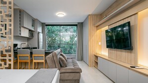 Ein modernes Wohnzimmer mit Sofa, Fernseher, Küchenzeile und einem Balkon mit Blick.