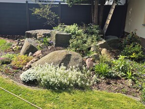 Ein Garten mit großen Steinen, verschiedenen Pflanzen und einer Rasenfläche.