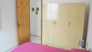 Um quarto com uma cama, um guarda-roupa e uma porta que dá para outro espaço.