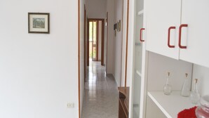 Um corredor com um quadro emoldurado à esquerda, portas de madeira e um armário branco com garrafas de vidro à direita.