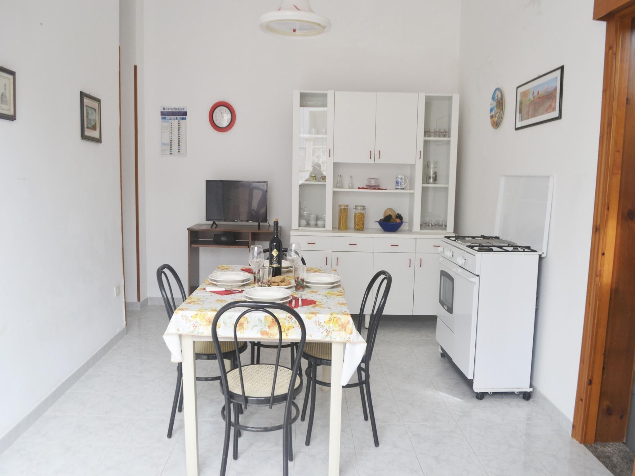 Uma cozinha compacta com área de refeições, armários brancos, fogão e televisão.