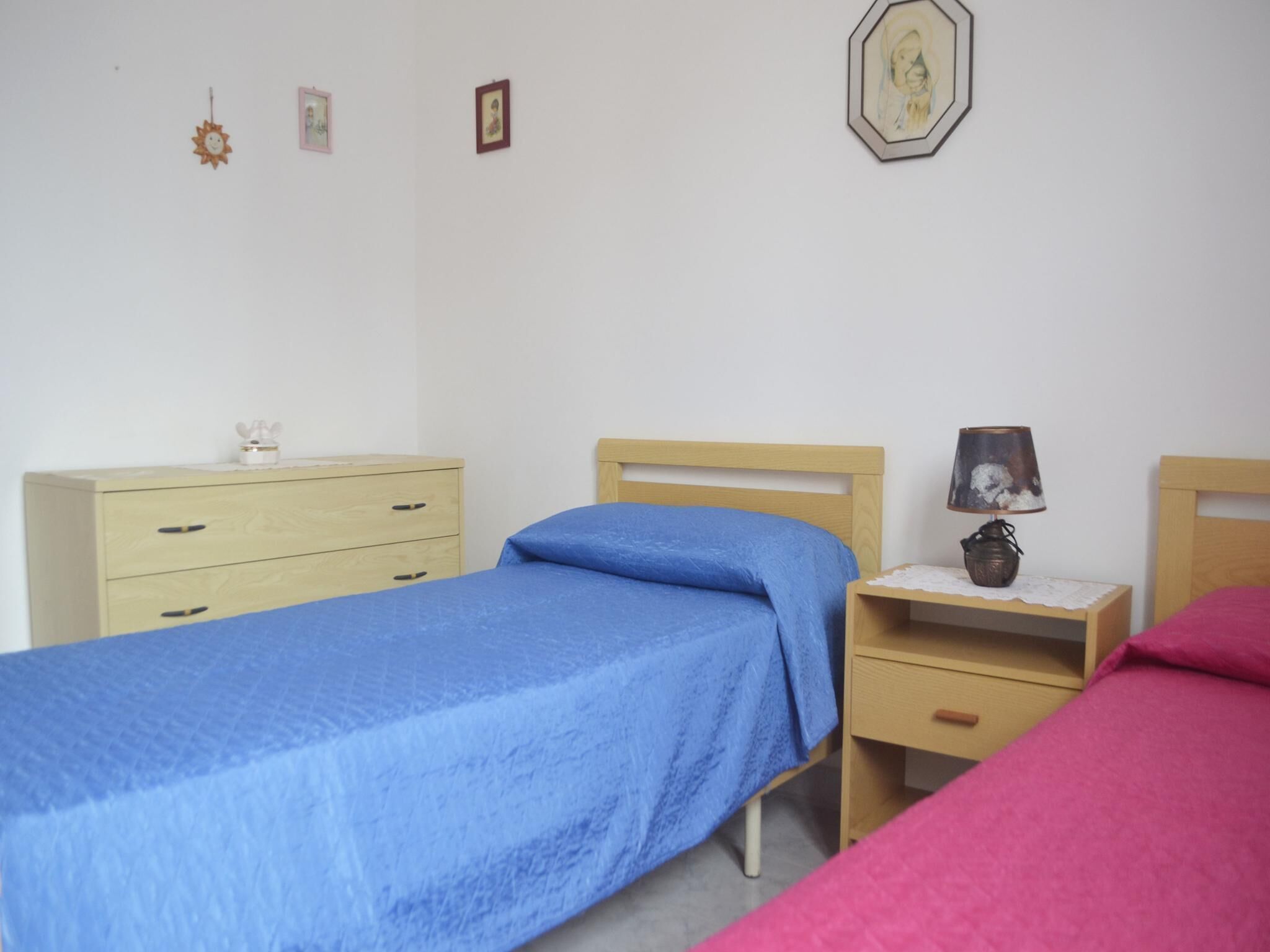 A bedroom with a single bed, a nightstand, a dresser, and a wall-mounted lamp.