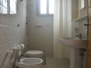 Et badeværelse med toilet, bidet og vask, flisebeklædte vægge og et vindue.