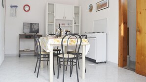 Uma sala de jantar com mesa, cadeiras, televisão, armários e geladeira.