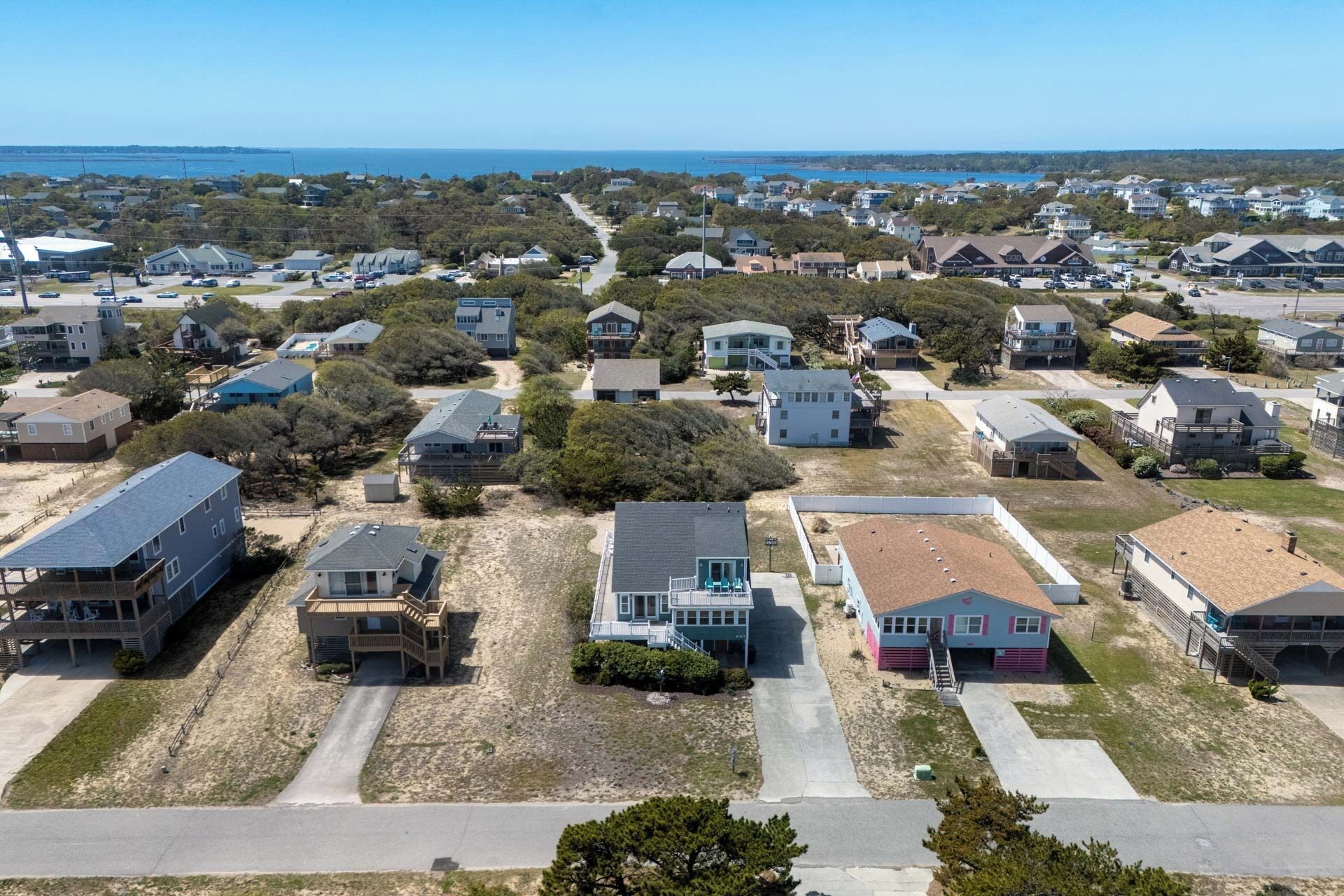 A residential area with houses, a road, and a beach in the background.