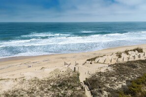 Una playa con un sendero arenoso que lleva al océano, barreras de madera y vegetación escasa.