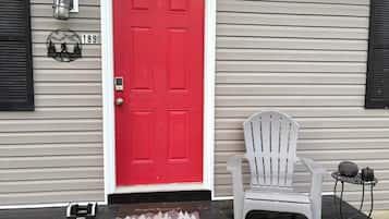 A red door with a mailbox and a white chair outside a house with siding.