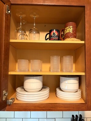 Un mueble de cocina con copas de vino, una taza y platos apilados.