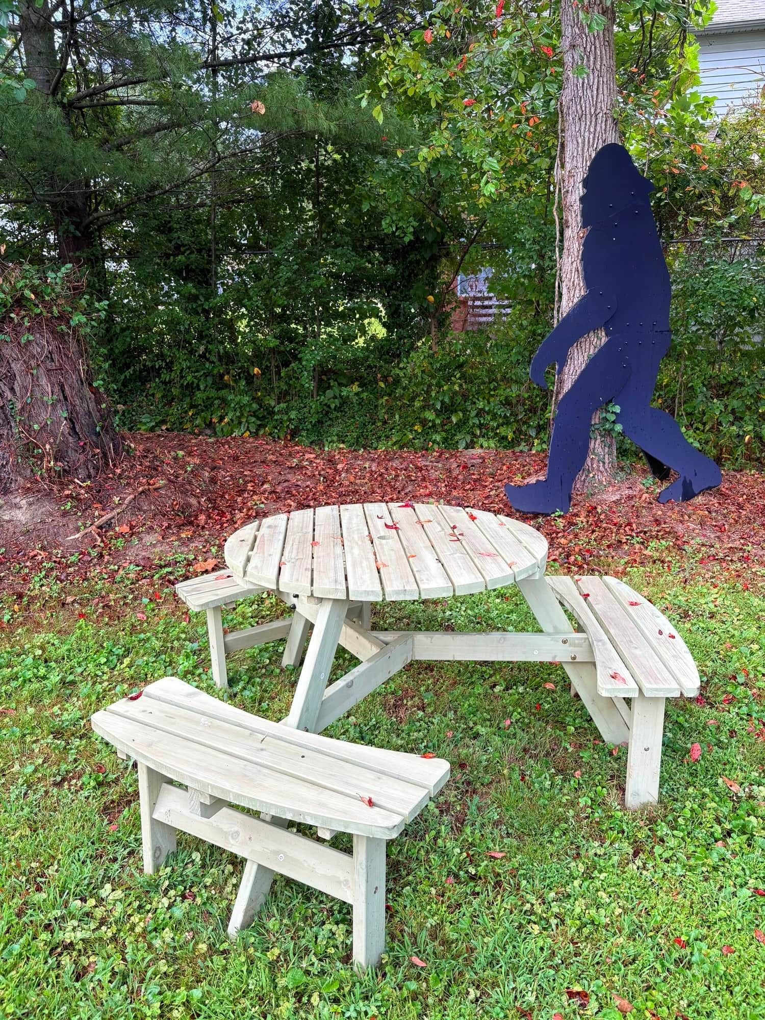 A picnic table set in a grassy area with a tree and shrubbery in the background.