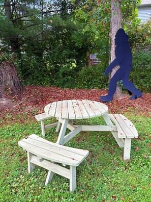 A picnic table set in a grassy area with a tree and shrubbery in the background. - Hide & Seek Lodge I Cozy 2BR I 15m to RRG I Wi-Fi (Stanton)