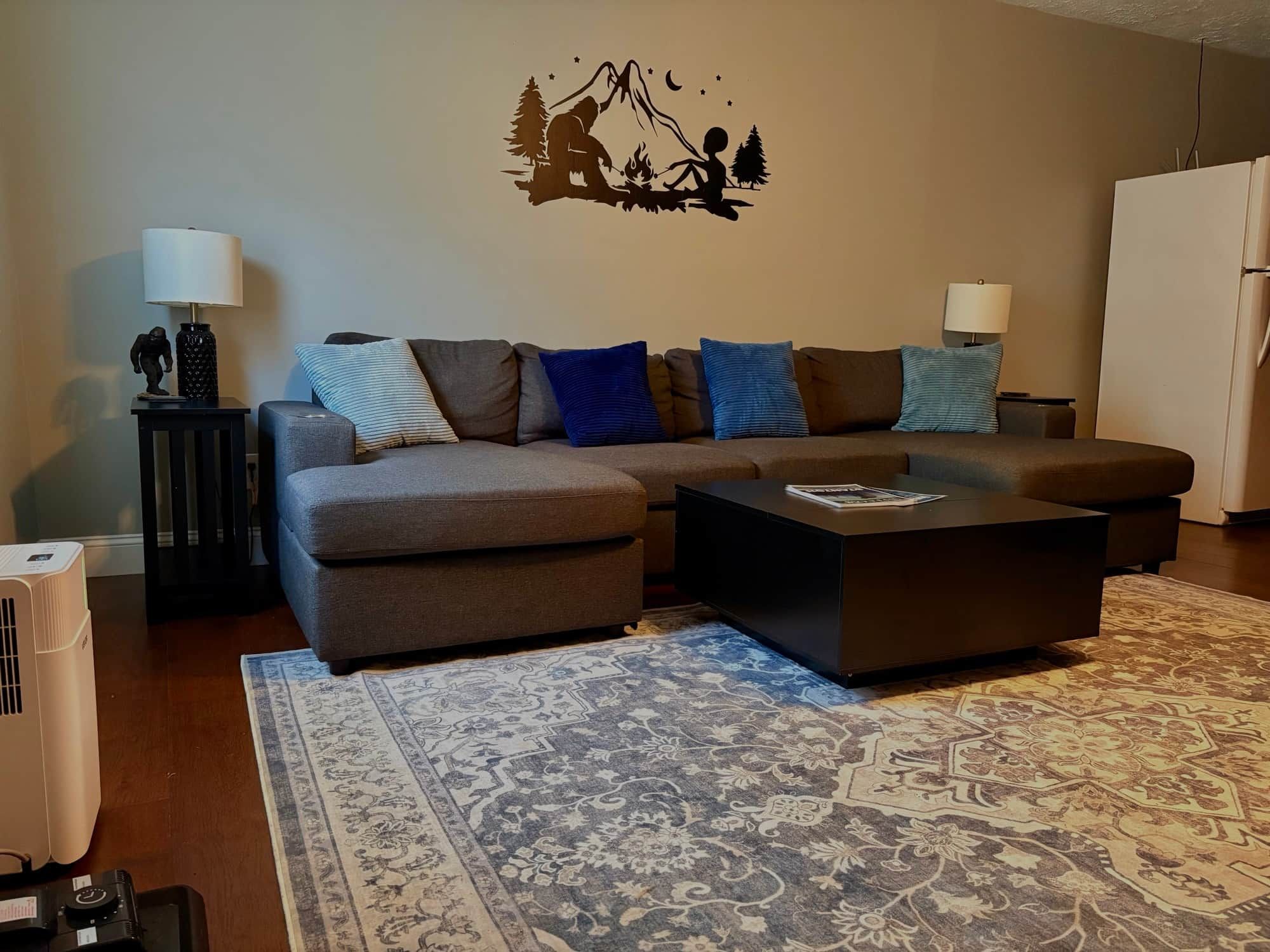 Ein Wohnzimmer mit einer Eckcouch, einem Couchtisch, einem gemusterten Teppich und einer Wanddekoration.