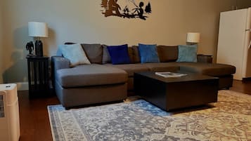 Ein Wohnzimmer mit einer Eckcouch, einem Couchtisch, einem gemusterten Teppich und einer Wanddekoration.