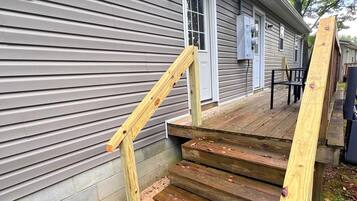A wooden staircase leading to a porch with a metal railing, a window, and a door on a gray siding house.