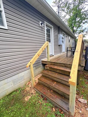 A wooden staircase leading to a porch with a metal railing, a window, and a door on a gray siding house. - Hide & Seek Lodge I Cozy 2BR I 15m to RRG I Wi-Fi (Stanton)