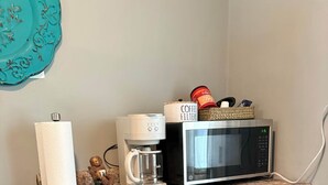 Et køkken med kaffemaskine, mikrobølgeovn og en kaffefilterkurv på bordet.