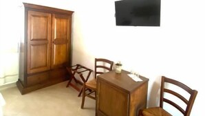 Una habitación con techo de madera, televisor montado en la pared, mueble de madera, mesa de comedor con sillas y suelo de baldosas.