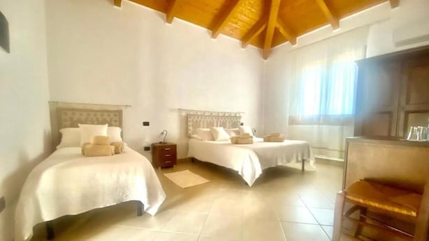 Una habitación de hotel con dos camas, techo de madera, un ventanal grande y una silla.