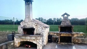 Dos hornos de piedra al aire libre con chimeneas, rodeados por un área empavedada.
