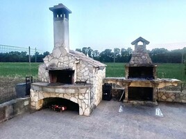 Due forni esterni in pietra con canne fumarie, circondati da una zona pavimentata.