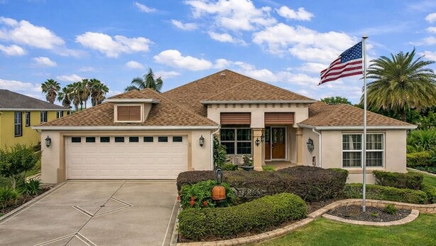 A single-story house with a garage, a front porch, and a flagpole with an American flag. - Luxury Golf Retreat w/pool in The Villages/Golf Cart Included/Prime Location (The Villages)