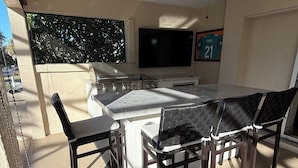 An outdoor kitchen area with a dining table and chairs, a ceiling fan, a TV mounted on the wall, and a sports jersey on the wall. - Luxury Golf Retreat w/pool in The Villages/Golf Cart Included/Prime Location (The Villages)