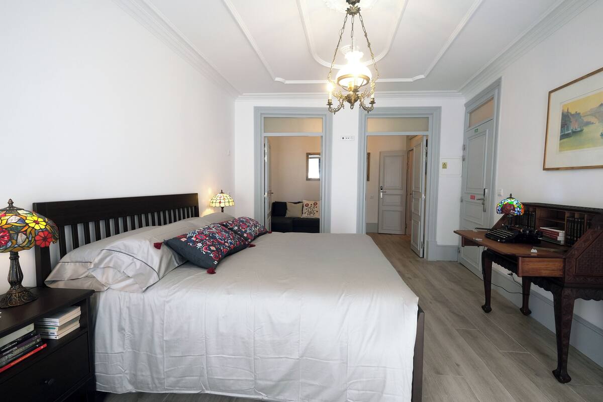 Une chambre à coucher avec un grand lit, un bureau avec une lampe et un lustre.