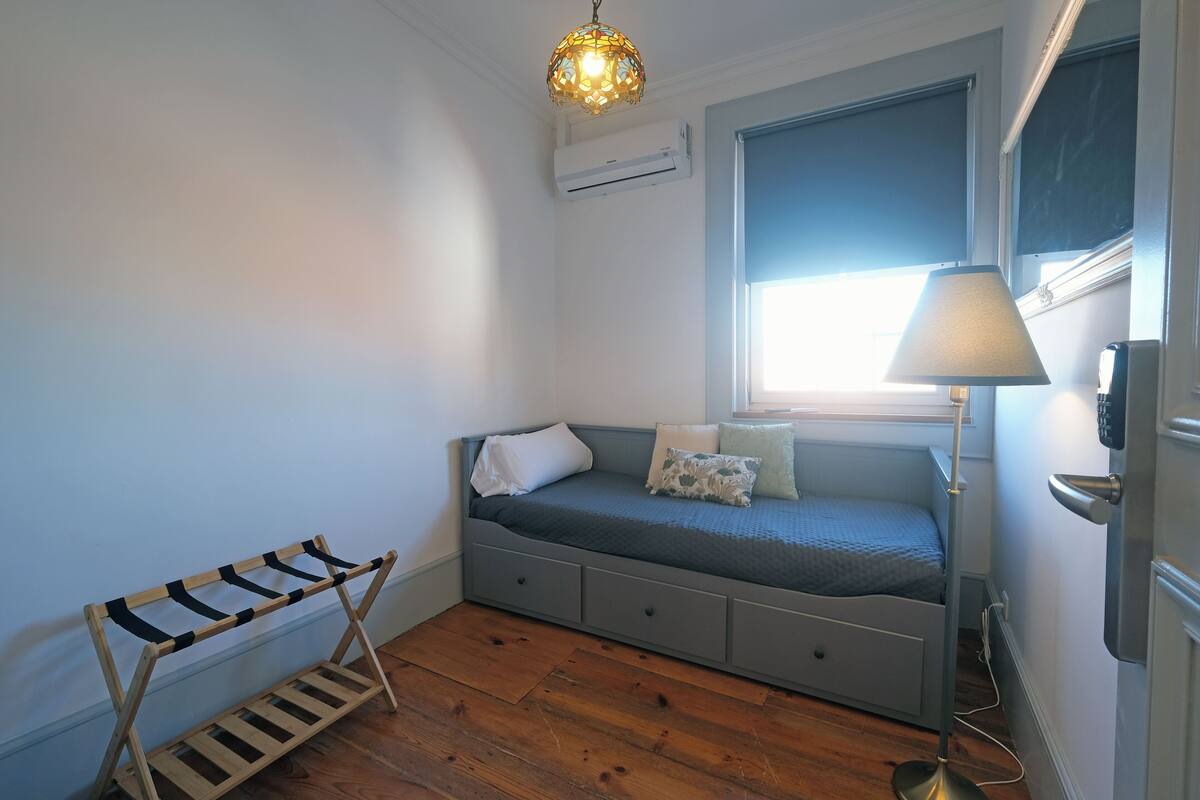 Une pièce comprenant un lit, une fenêtre, un luminaire suspendu et un climatiseur fixé au mur.