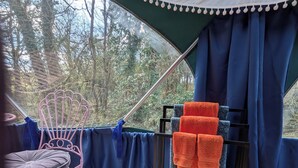 Una habitación con tienda de campaña, una silla, una mesita y un perchero con toallas.