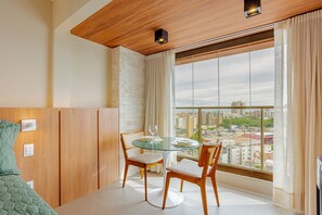 A modern room with a glass table, two wooden chairs, a bed, a city view, and a wooden ceiling. - RV12 Beautiful and Cozy Studio in Rio Vermelho (Salvador)