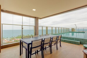 Een balkon met een eettafel en stoelen, met uitzicht op een zwembad en de oceaan.