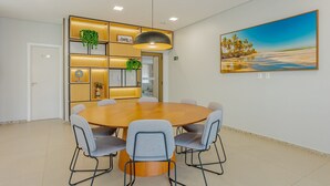 Et moderne spiseområde med et rundt bord, seks stole, en hængende lampe, et billede på væggen og indbyggede hylder med planter.
