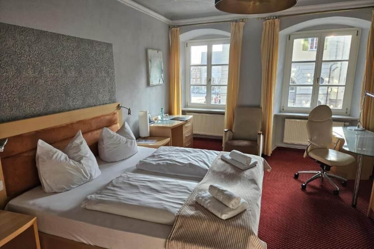 A hotel room with a large bed, a desk, a chair, and a window with curtains.