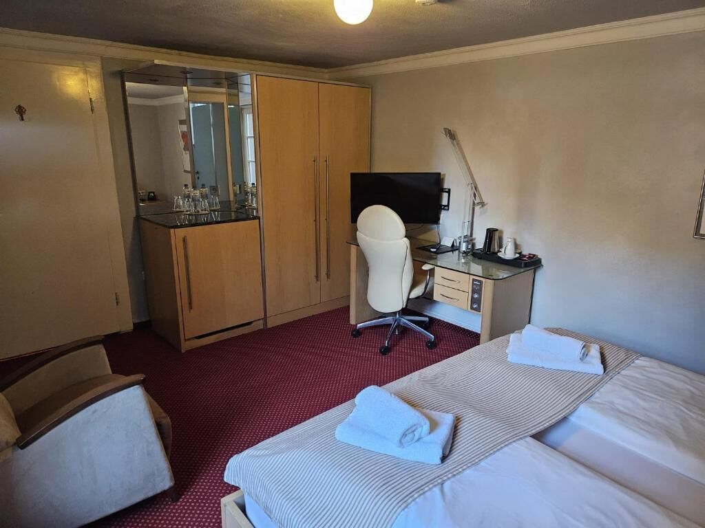 A hotel room with a bed, a desk, a chair, a television, and a wardrobe.
