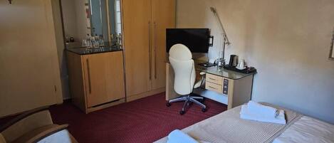 Ein Hotelzimmer mit Bett, Schreibtisch, Stuhl, Fernseher und Kleiderschrank.