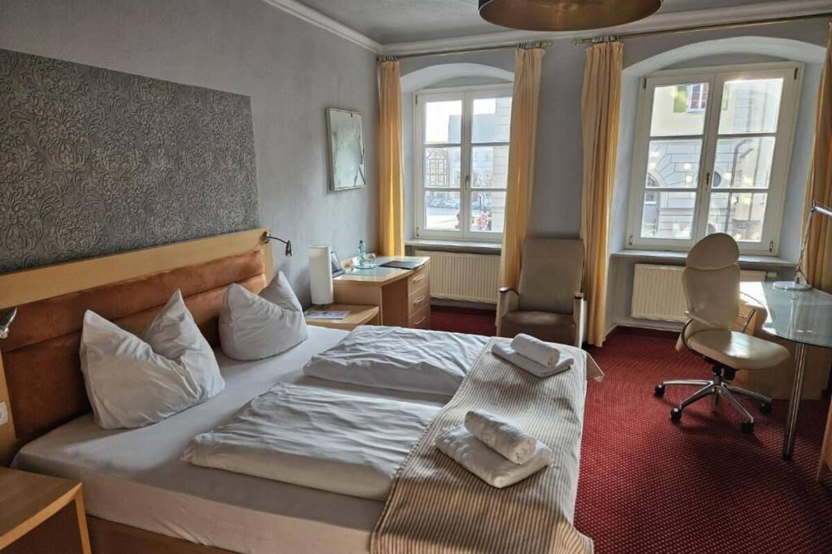 A hotel room with a large bed, a desk, a chair, and a window with curtains.