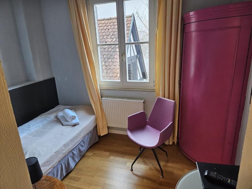 A bedroom with a bed, a chair, a wardrobe, a window, and a radiator.