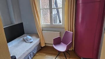 A bedroom with a bed, a chair, a wardrobe, a window, and a radiator.