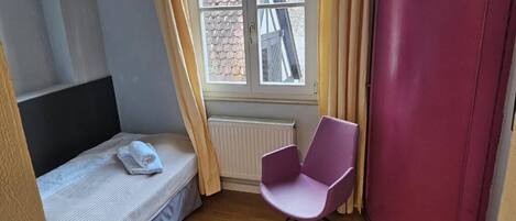 A bedroom with a bed, a chair, a wardrobe, a window, and a radiator.