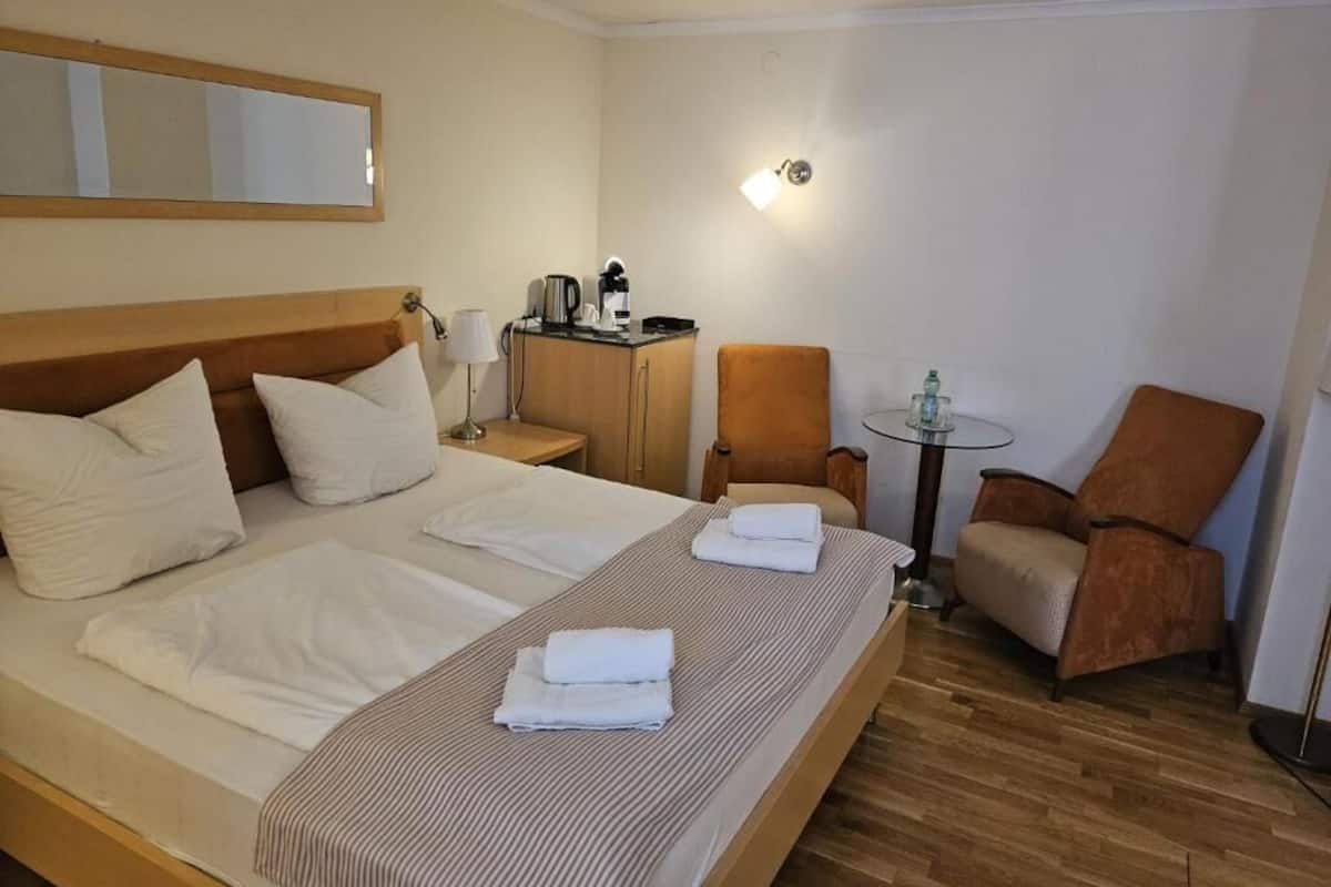 A hotel room with a bed, two chairs, a small table, a lamp, and a coffee machine.