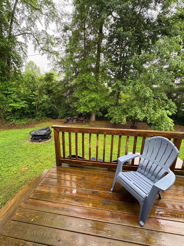 A wooden deck with a gray Adirondack chair, a wooden railing, and a pile of firewood.