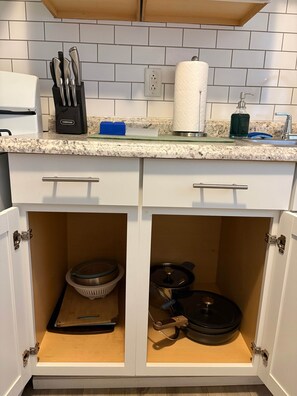 Ett kök med vita skåp, en bänkskiva i granit, ett knivblock, en hållare för hushållspapper och en diskho.