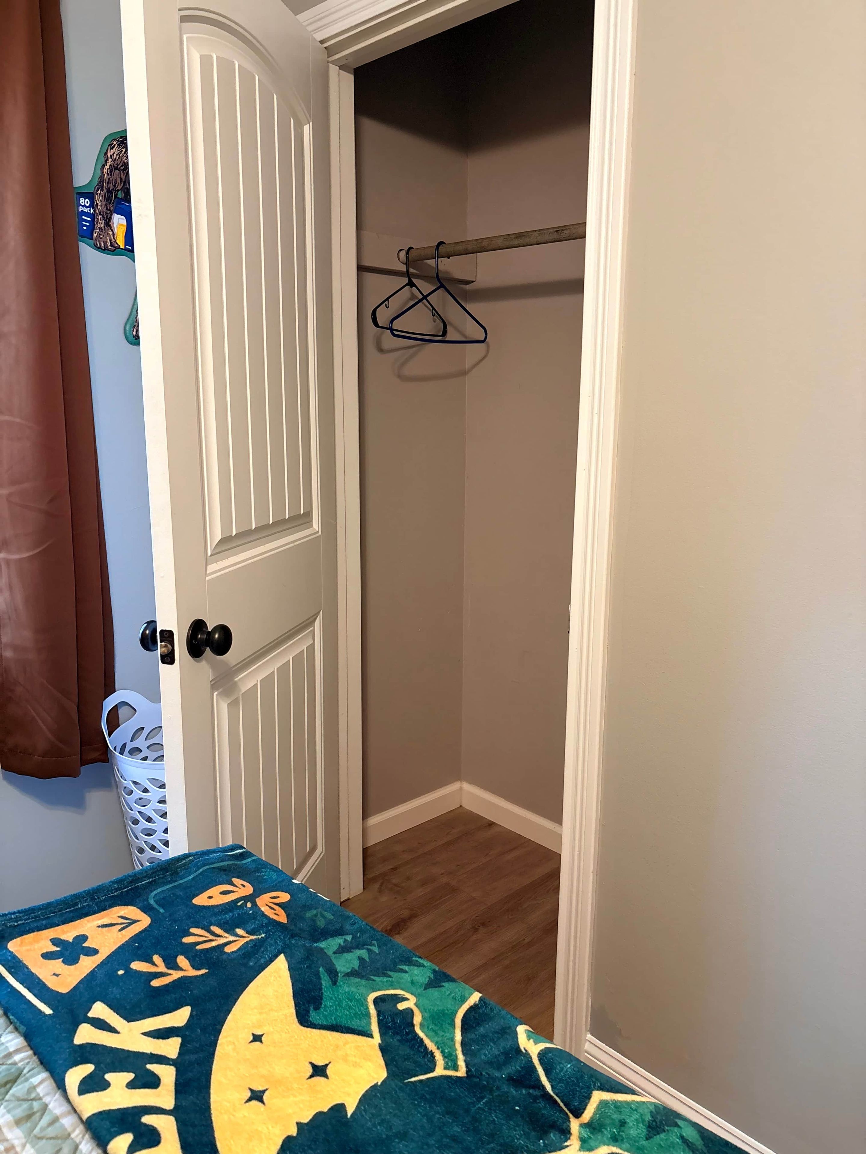 A room with a door, a coat rack, a blue and yellow blanket, and a white basket.