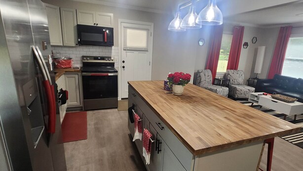 Una cocina moderna con electrodomésticos de acero inoxidable, una isla de madera y un comedor con sofá y mesa.