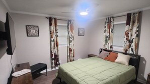 Un dormitorio con cama, mesitas de noche, un banco, alfombra y cortinas.