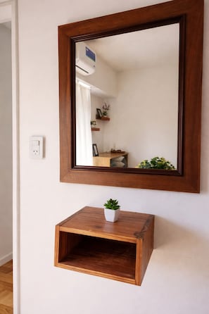 A mirror with a wooden frame, a small wooden shelf below it, and a potted plant on the shelf. - Studio apartment in Palermo (Buenos Aires)